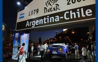 Med ryggen til i blå skjorte tager VW Motorsportsdirektør Kris Nissen imod Carlos Sainz’s co-driver Michel Perin i forbindelse med den ceremonielle start til årets Rallye Dakar i Buenos Aires.