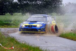Karl-Åge Jensens Subaru Impreza World Rally Car runder et skarpt sving i silende regnvejr og vælter en dækstabel i samme øjeblik.